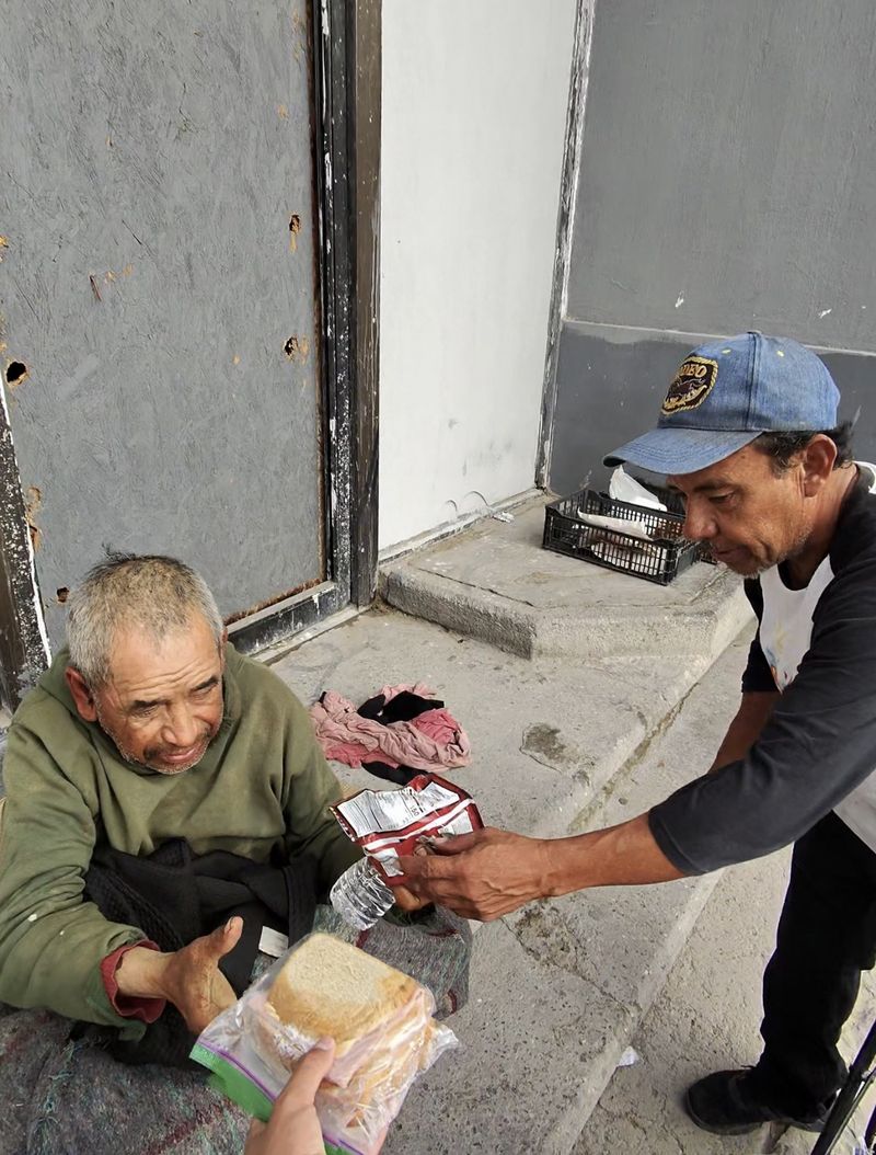 A man on a sidewalk holding a meal and water bottle from an outreach visit