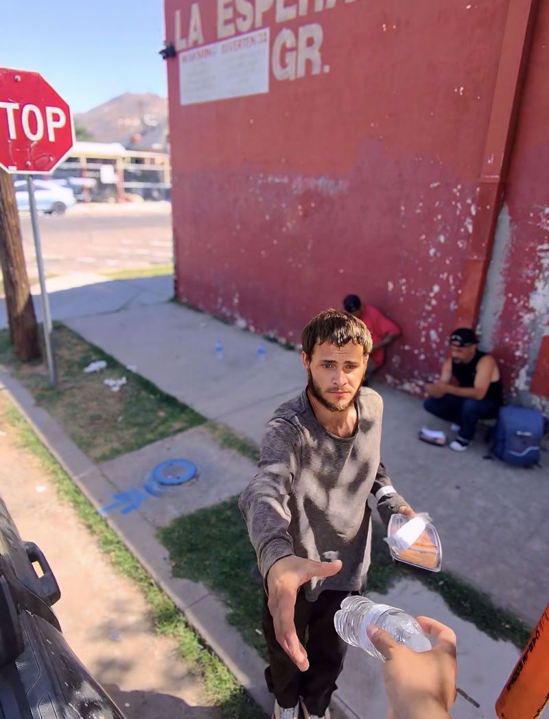 A volunteer reaching out to hand water and a meal to a man near a stop sign