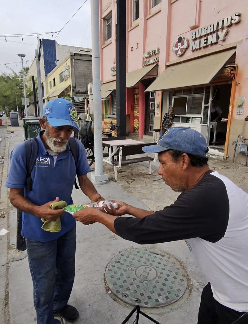 Two men exchanging a water bottle and supplies on a city sidewalk